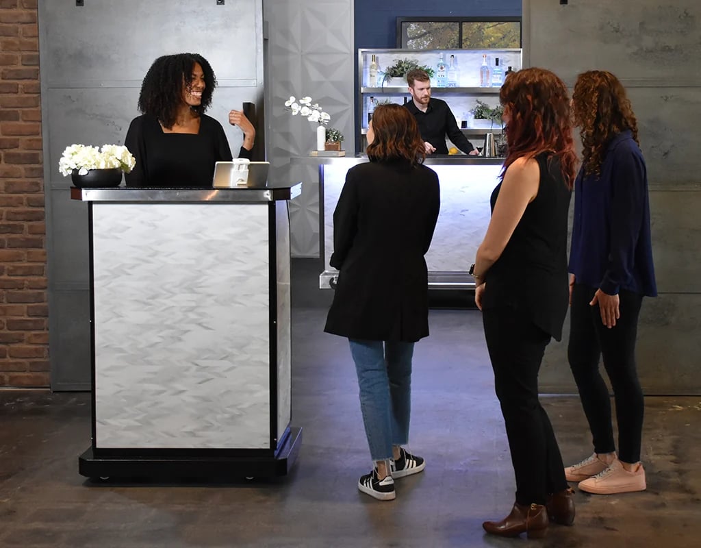 A smiling restaurant host greeting arriving guests at the host stand