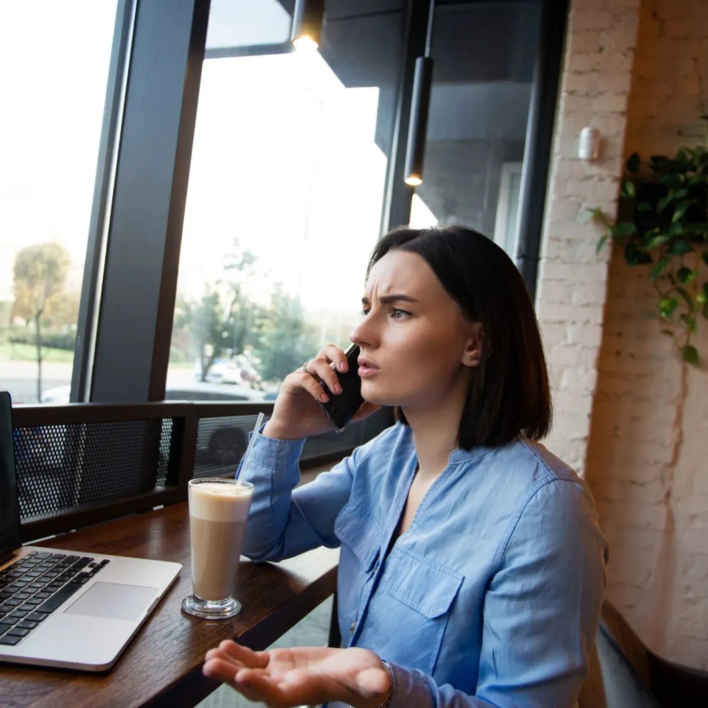 A restaurant operator on the phone at a café table with a laptop, looking concerned