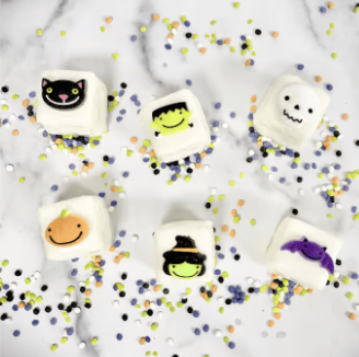 White petite fours decorated with Halloween faces — a cat, Frankenstein, ghost, pumpkin, witch hat, and bat