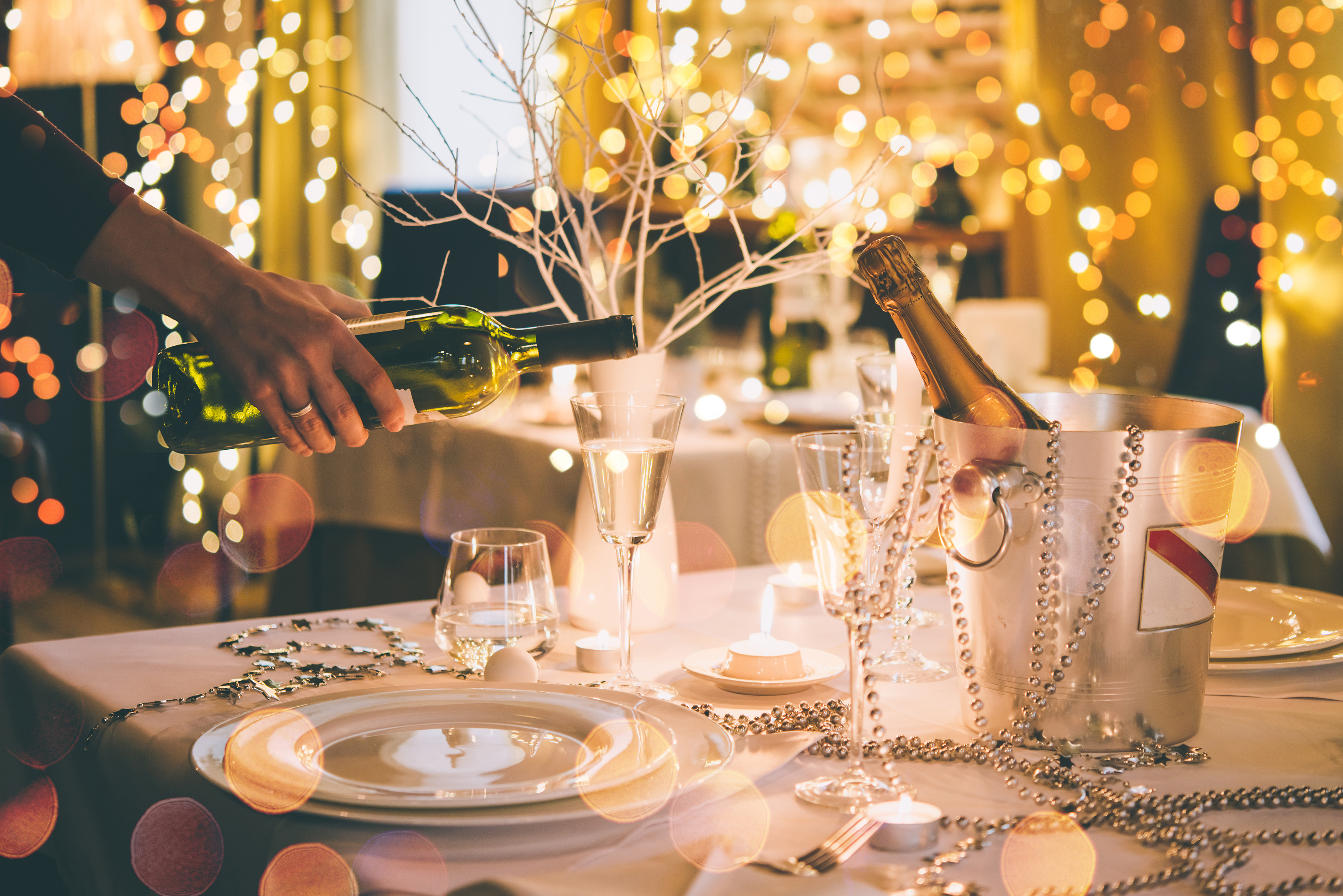 A festive holiday table set with wine and champagne glasses and string lights